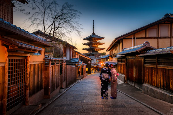 A Kyoto street with traditional wooden buildings and a pagoda at dusk